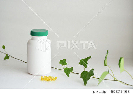 サプリメントの白いボトルと黄色いソフトカプセルの写真素材