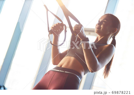 Working hard. Side view of a young strong and fit woman exercising with fitness trx straps at gym Working hard. Side view of a young strong and fit woman exercising with fitness trx straps at gym 69878221