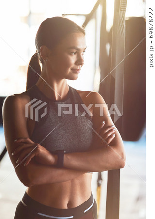 Vertical shot of young attractive fit woman wearing sportswear keeping arms crossed and looking away while standing at gym Vertical shot of young attractive fit woman wearing sportswear keeping arms crossed and looking away while standing at gym 69878222