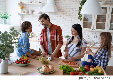 Preparing a salad. Lovely family of four cooking together in the modern kitchen at home 69878774
