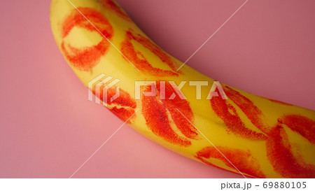 Red lipstick on a yellow banana on a pink background. 69880105