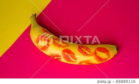 Red lipstick on a yellow banana on a pink background. 69880116