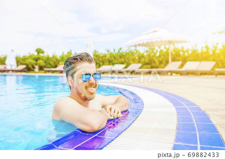 A man looks out of the pool, hanging on the railing. 69882433