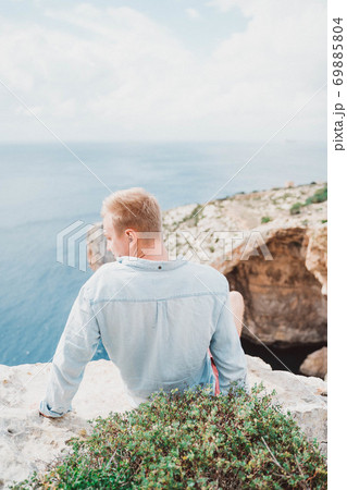 A man seating in front of a large rock. Watching to the sea. Nice weather. A man seating in front of a large rock. Watching to the sea. Nice weather. 69885804