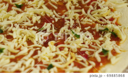 Cooking pizza. Chef put cheese and basil on the base of the pizza greased with tomato paste. A man Cooking pizza. Chef put cheese and basil on the base of the pizza greased with tomato paste. A man 69885868