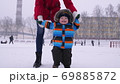 Mother leads the hands of a small smiling baby in the snow in the park. The first steps of the child 69885872