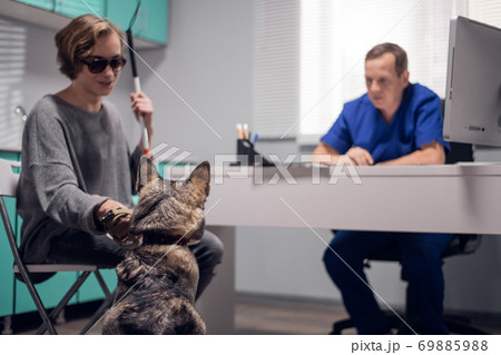 A blind person with a guide dog having an appointment at a vet clinic A blind person with a guide dog having an appointment at a vet clinic 69885988