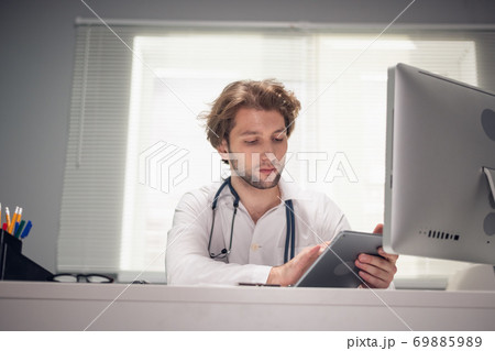 A portrait of a doctor sitting with a digital tablet at his desk, checking messages, making corrections in the schedule A portrait of a doctor sitting with a digital tablet at his desk, checking messages, making corrections in the schedule 69885989
