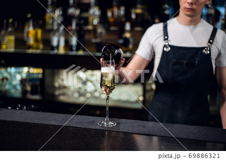 a young bartender pours champagne into a glass from a bottle on the bar a young bartender pours champagne into a glass from a bottle on the bar 69886321