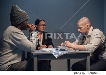 A beautiful woman lawyer with glasses gets acquainted with the evidence during the interrogation of her client a black drug addict A beautiful woman lawyer with glasses gets acquainted with the evidence during the interrogation of her client a black drug addict 69886338