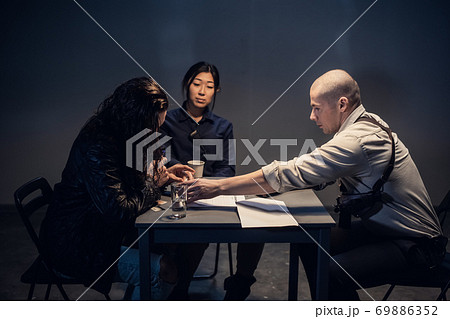 A police investigator with a gun in a holster meets with a man suspected of theft in the presence of a lawyer at the police station. 69886352
