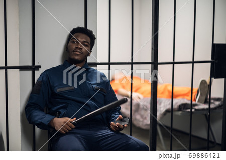 A prison warden guards cells with prisoners sentenced to life in orange prison uniforms. A prison warden guards cells with prisoners sentenced to life in orange prison uniforms. 69886421