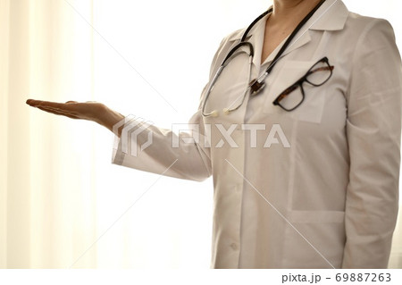 The doctor in a white robe stands with her arm outstretched and an empty palm showing anything. The doctor in a white robe stands with her arm outstretched and an empty palm showing anything. 69887263