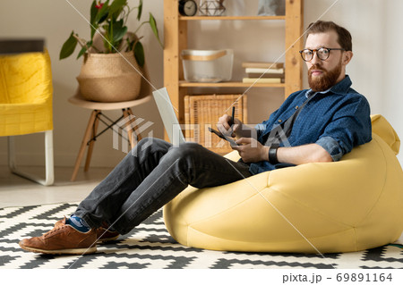 Young male freelance designer in eyeglasses and casualwear looking at you 69891164