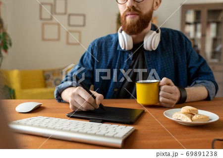Young creative web designer in casualwear having coffee with cookies and drawing Young creative web designer in casualwear having coffee with cookies and drawing 69891238