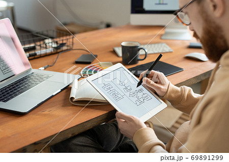 Young bearded freelance programmer holding stylus over touchscreen Young bearded freelance programmer holding stylus over touchscreen 69891299