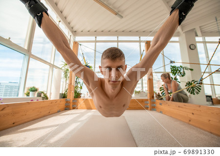 Sportsman hanging over the floor with arms and legs fixed with special equipment Sportsman hanging over the floor with arms and legs fixed with special equipment 69891330