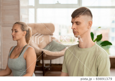 Young relaxed sportsman in activewear keeping eyes closed while meditating 69891379