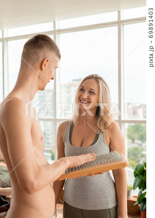 Young blond pretty sportswoman looking at her fitness trainer touching yoga pad Young blond pretty sportswoman looking at her fitness trainer touching yoga pad 69891403
