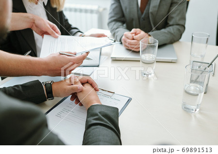 Hands of contemporary business partners over documents sitting by table at break Hands of contemporary business partners over documents sitting by table at break 69891513