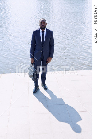Young African businessman in formalwear holding black leather handbag 69891637