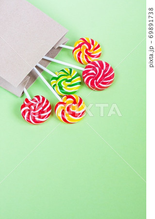 Colorful lollipops in paper bag on green background. Sweets for party. Sugar 69891738