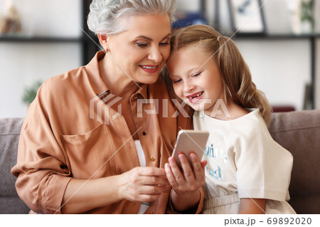 Happy grandmother sharing media on smartphone with granddaughter. 69892020