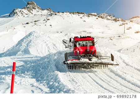 Red modern snowcat ratrack with snowplow snow grooming machine preparing ski slope piste hill at alpine skiing winter resort Ischgl in Austria. Heavy machinery mountain equipment track vehicle 69892178