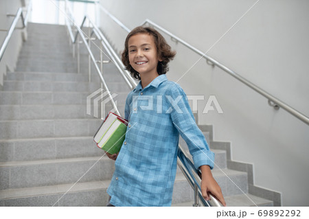 Happy schoolboy standing on stairs, holding pile of books 69892292