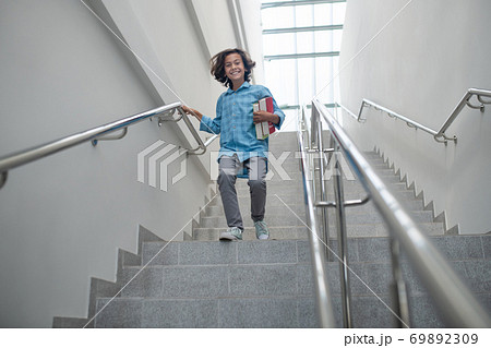 Excited schoolboy holding pile of books, running downstairs Excited schoolboy holding pile of books, running downstairs 69892309