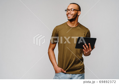 Portrait of a young african american man wearing green t-shirt holding tablet pc pad Portrait of a young african american man wearing green t-shirt holding tablet pc pad 69892372