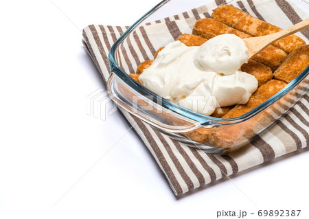 tiramisu dessert cooking - Traditional Italian Savoiardi ladyfingers Biscuits and cream in glass baking dish isolated on white with clipping path 69892387