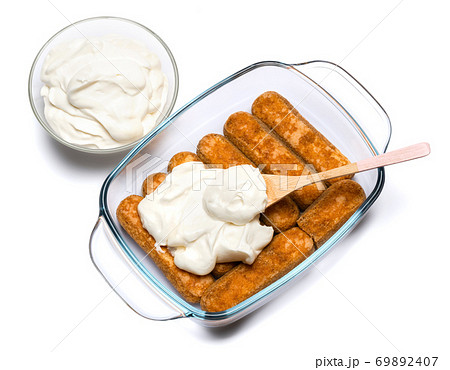 tiramisu dessert cooking - Traditional Italian Savoiardi ladyfingers Biscuits and cream in glass baking dish isolated on white with clipping path 69892407