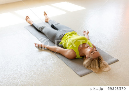 Fit adult woman lying on the mat in shavasana and practice yoga nidra the studio indoor, side front view, selective focus. Fit adult woman lying on the mat in shavasana and practice yoga nidra the studio indoor, side front view, selective focus. 69893570
