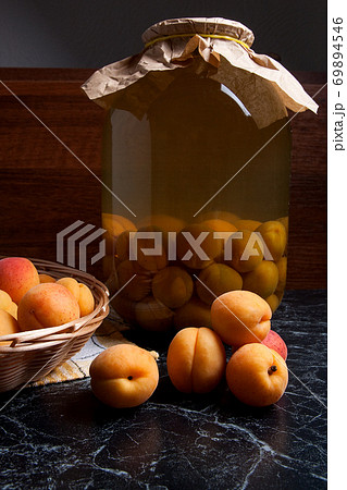 Fresh organic harvested apricots in basket and big glass jar with canned apricot compote on dark marble.. Fresh organic harvested apricots in basket and big glass jar with canned apricot compote on dark marble.. 69894546