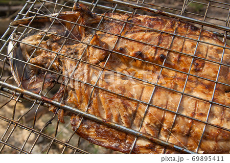 Close up view of fresh fish with sauce cooked on an open flame grill.. 69895411