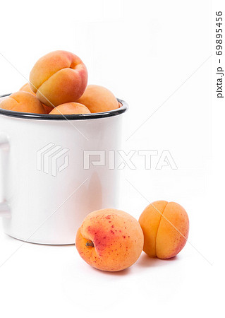 Harvested apricots in white cup with whole and halved apricots on white background.. Harvested apricots in white cup with whole and halved apricots on white background.. 69895456