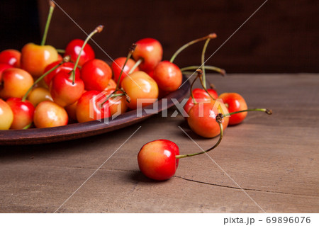 Clay plate with yellow sweet cherry on wooden background. 69896076