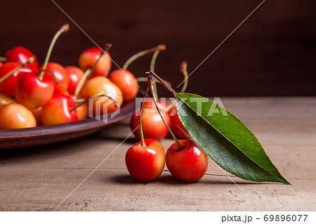 Clay plate with yellow sweet cherry on wooden background. 69896077