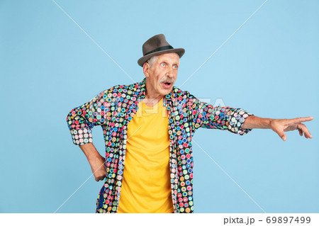 Senior hipster man in stylish hat isolated on blue background. Tech and joyful elderly lifestyle concept Senior hipster man in stylish hat isolated on blue background. Tech and joyful elderly lifestyle concept 69897499