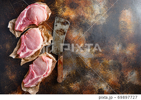Bunch Pork steaks, fillets for grilling, baking or frying, Pork with ribs. Tenderloin. Entrecote warped in paper with butcher cleaver on side over rustic metall table top view space for text 69897727