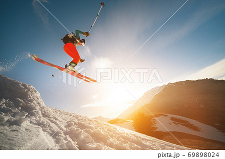 Professional athlete young male skier with a backpack and in a ski mask makes a trick in flight after jumping from a kicker on the background of a sunset Professional athlete young male skier with a backpack and in a ski mask makes a trick in flight after jumping from a kicker on the background of a sunset 69898024