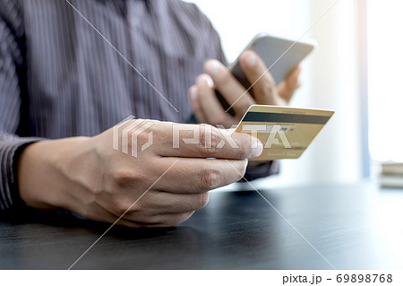 The businessman's hand is holding a credit card and using a smartphone for online shopping and internet payment in the office 69898768