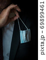 The man takes a disposable medical mask out of his pocket instead of a napkin. A man with a disposable mask in a suit. Respiratory protection. 69899461