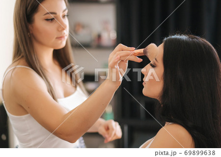 Makeup artist work in her beauty studio. Portrait of Woman applying makeup. Professional make up master. Beautiful make up artist start making a makeup for brunette woman 69899638