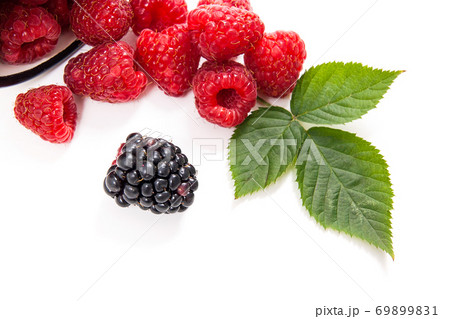 White cup with ripe raspberries with green leaf and one blackberry isolated on white background. 69899831