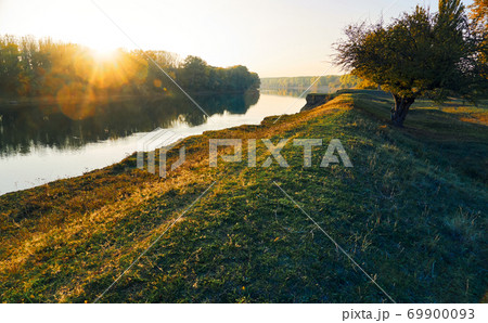colorful autumn forest landscape at sunset, trees near river and sky, bright sunlight reflected in water colorful autumn forest landscape at sunset, trees near river and sky, bright sunlight reflected in water 69900093