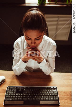 Female office worker sits at her desk with her fingers crossed. Woman looking at computer keyboard on the table. High quality photo 69904353