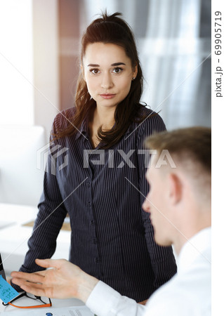 Business woman and man discussing questions while using computer at workplace in sunny office Business woman and man discussing questions while using computer at workplace in sunny office 69905719