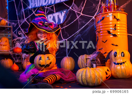 Little beautiful girl in a witch costume celebrates Happy Halloween party in interior with pumpkins Little beautiful girl in a witch costume celebrates Happy Halloween party in interior with pumpkins 69906165